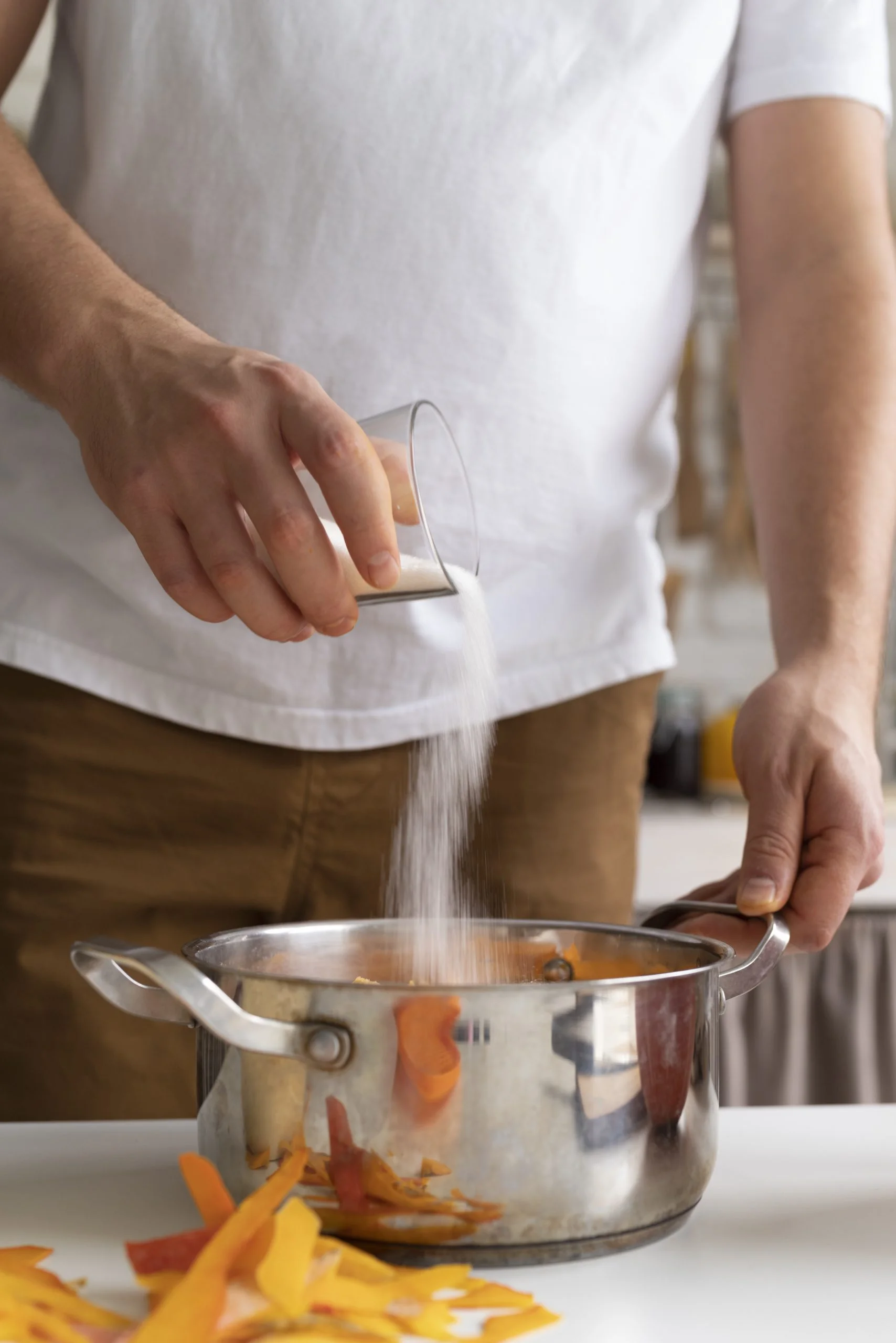 Your Heart Health. A person pouring a large amount of white salt into a cooking pot, illustrating high sodium consumption